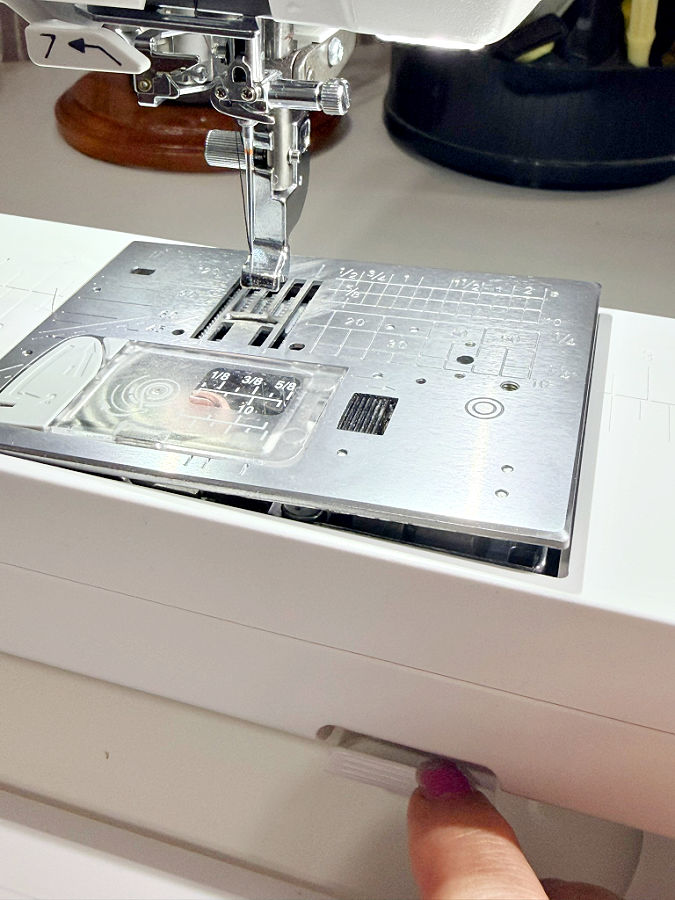 a womans finger shown while pressing the button topop up the throat plate on a modern sewing machine