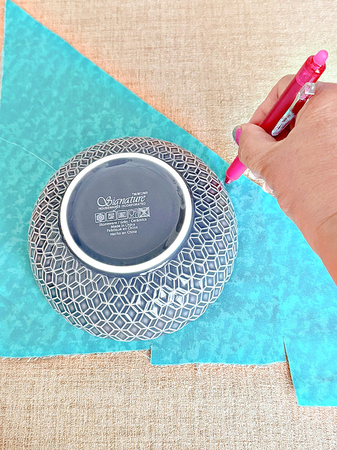 a plate is used to trace a circle on a piece of fabric a womans hand holds a pen while drawing