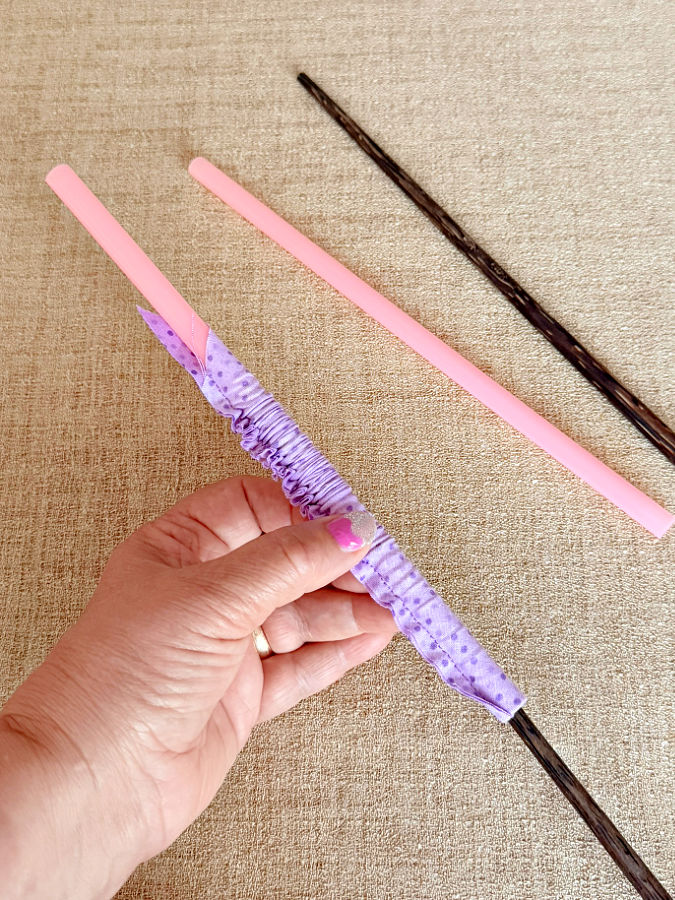 a womans hand holds a drinking straw a chopstick is used to turn a fabric tube on the straw