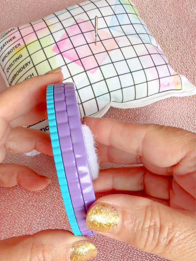 a woman holds the needle noter showing the three separate discs a needle pillow in the background