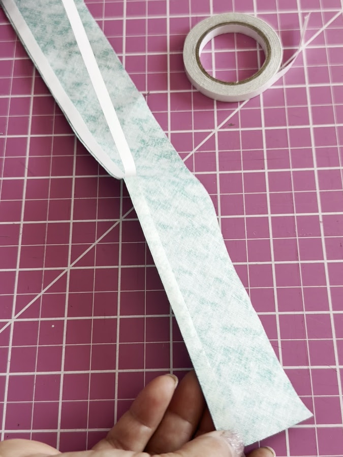 a womans hand holding a piece of material with wonder tape attached a roll of wonder tape in the background
