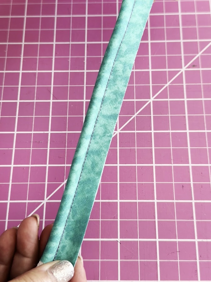 a womans hand holds a piece of material with the thick cord sewn inside the piping