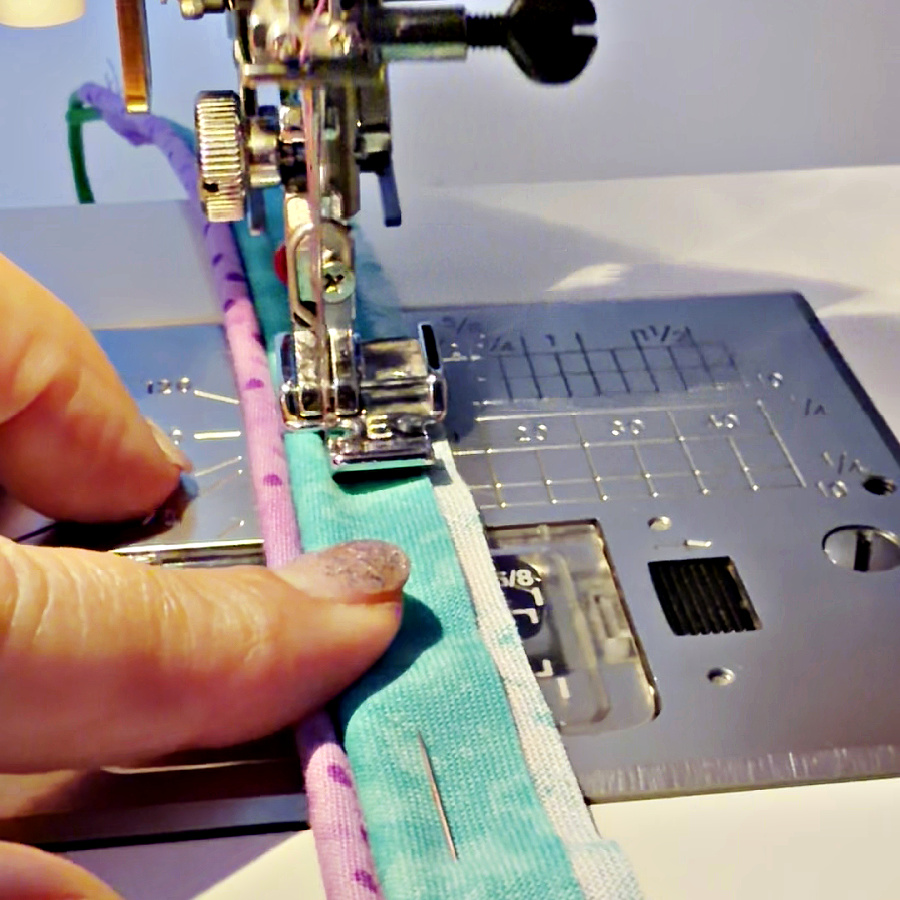 a womans hand guiding a section of piping to sew on another piece of material using a zipper foot for sewing