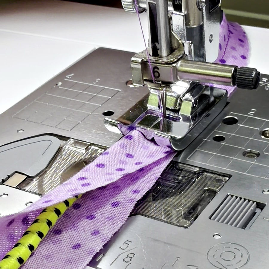 a sewing machine needle assembly shown while sewing a thick yellow cord in a piece of material