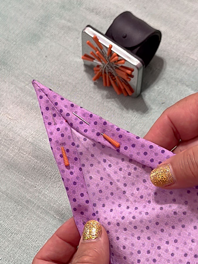 a woman holds the fabric with the corner seen from the wrong side pins installed for further finishing the hem
