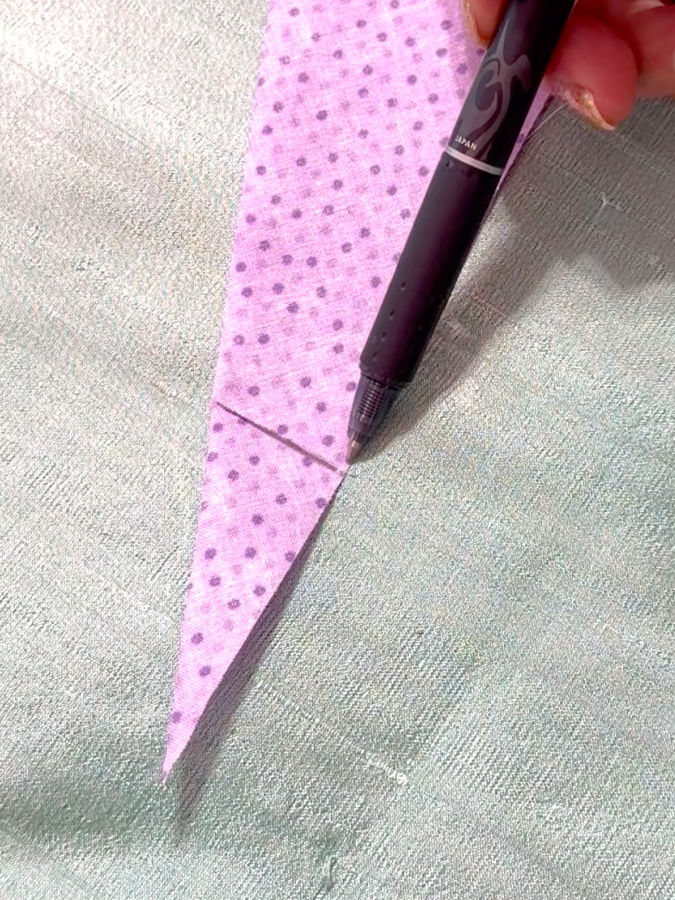 a woman holds a [pen after drawing the first reference line on the fabric