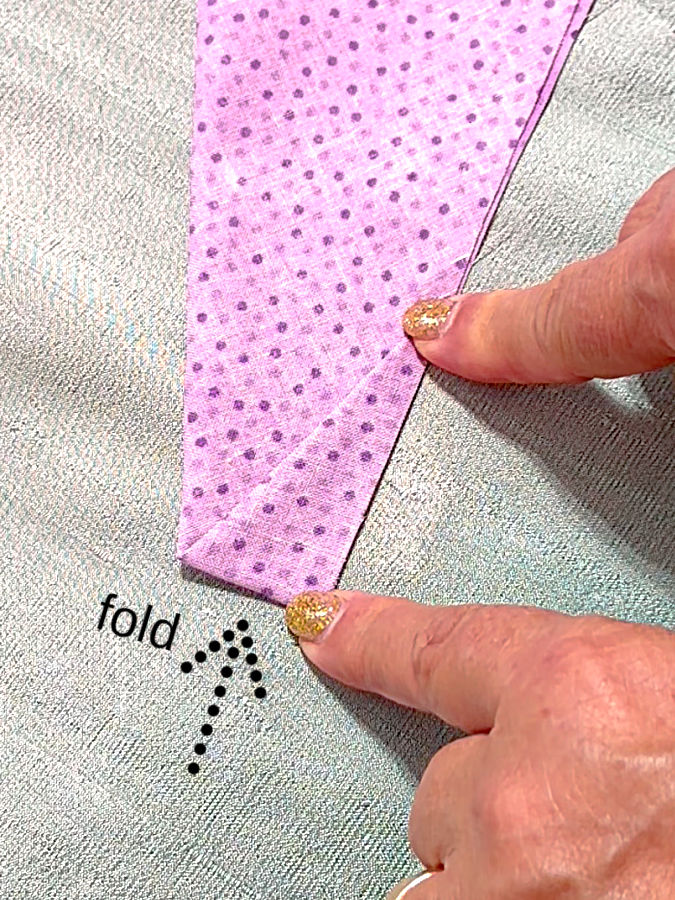 a womans hands folding the fabric and aligning the edges an arrow points to the fold line