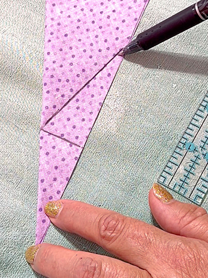 a womans hand holds the corner of the fabric the line marked previously visible on the fabric a ruler and a pen also in the image