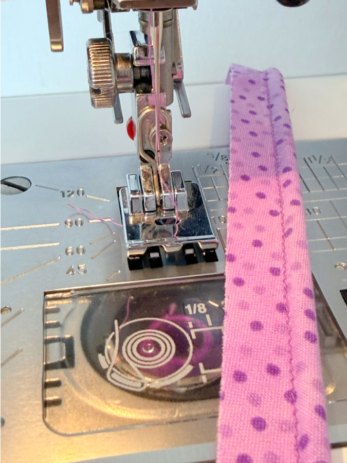 a piece of material with the thin cord sewn inside the piping a sewing machine needle assembly in the background