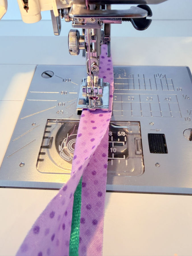 a sewing machine needle assembly shown while sewing a thin green cord in a piece of material