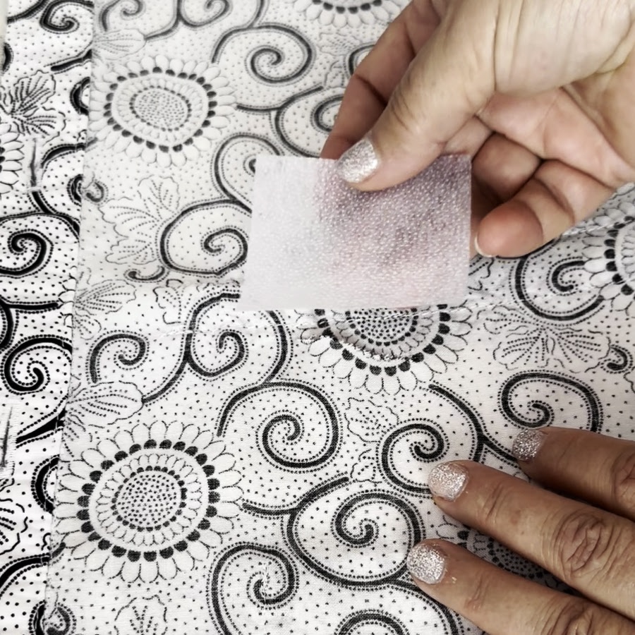 a womans hands holding a rectangular piece of fusible interfacing over the area with a hole