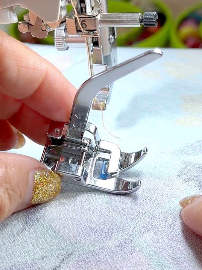 a womans hand holds the knit presser foot for inspection the foot support assembly of a srewing machine in the background