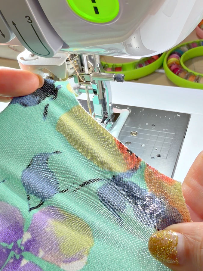 a womans hands holding a piece of lightweight rayon knit a sewing machine needle assembly in the background