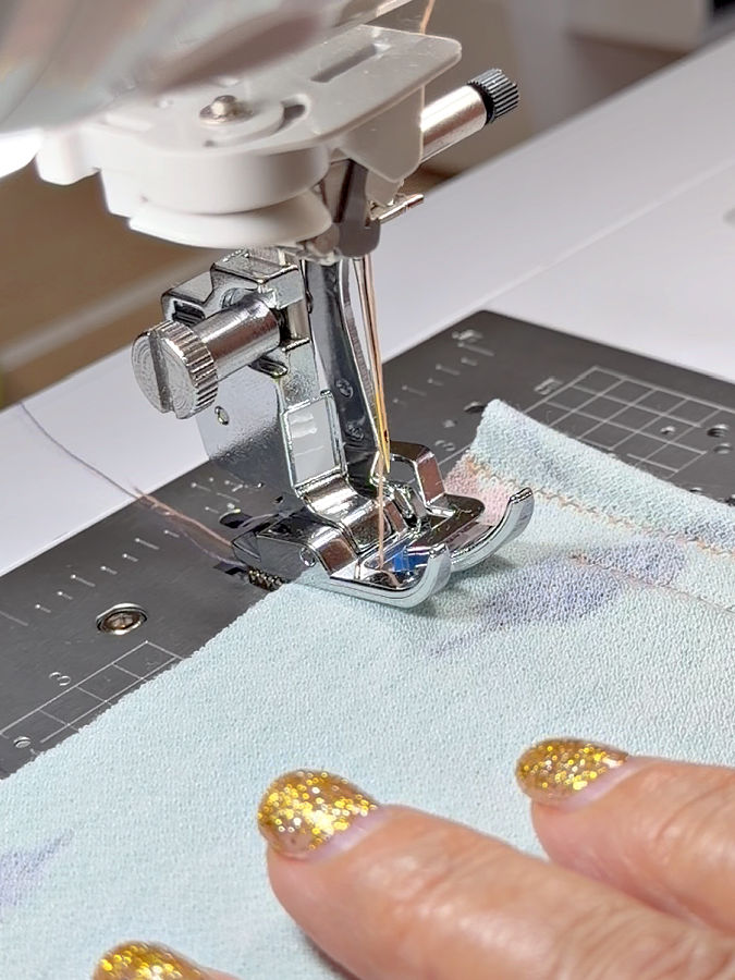 the knit presser foot installed in a sewing machine at the edge of the fabric a womans hand guides the fabric