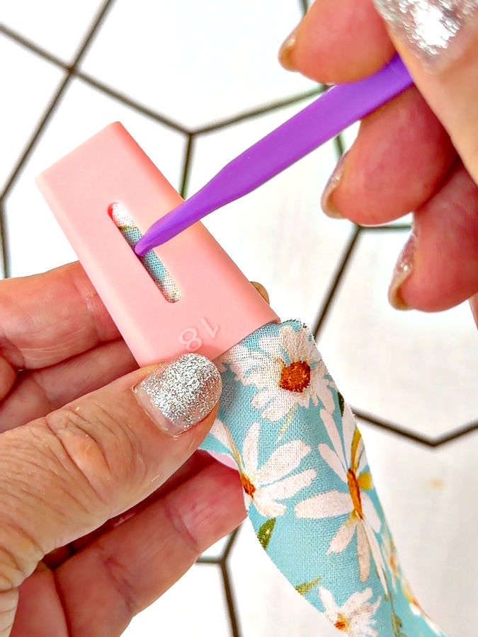 a woman uses a tool to push the fabric into the bias tape maker