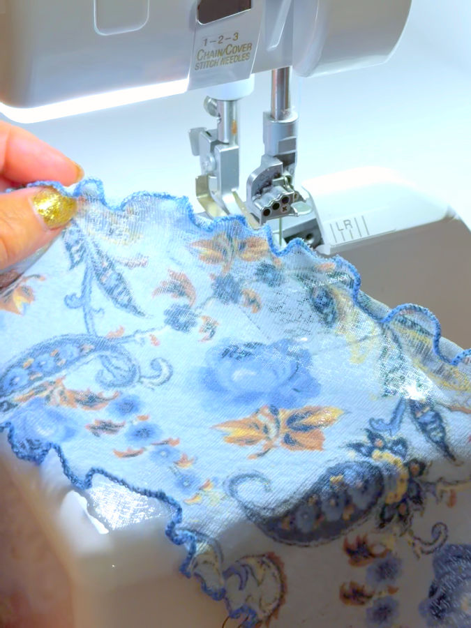 a woman holds a piece of thin fabric with a lettuce hem near the needle assembly of a serger