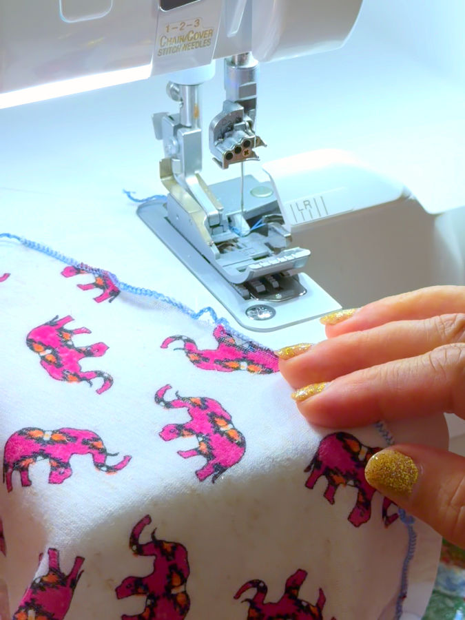 a woman guides a piece of fabric with an elephant print towards the needle assembly of a serger