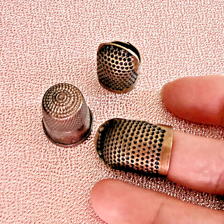 a womans hand with a thimble on one finger two other thimbles in the background