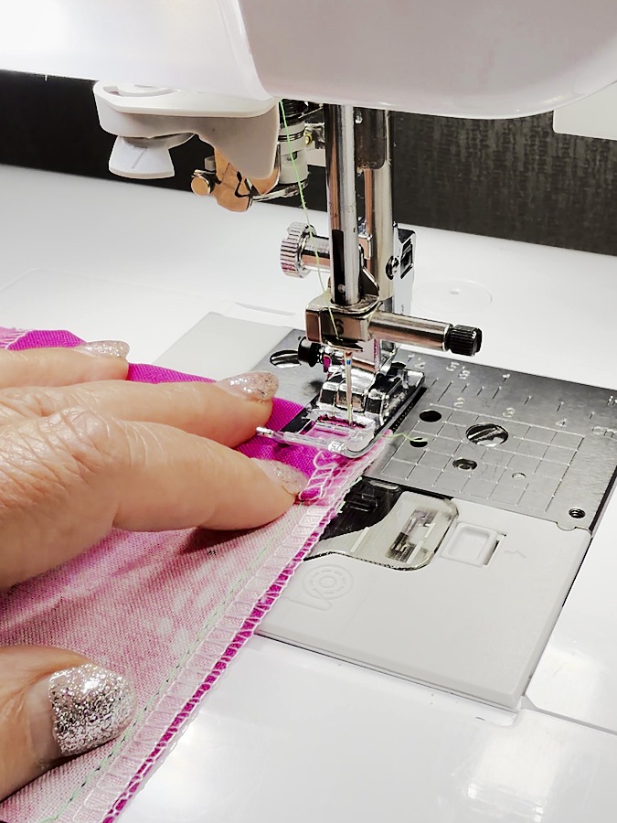 a womans hand guides the material for sewing the seam to join the insert to the original piece