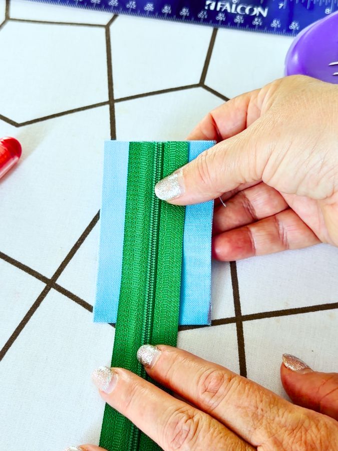 a woman holds a zipper over the rectangle of fabric positioning it properly