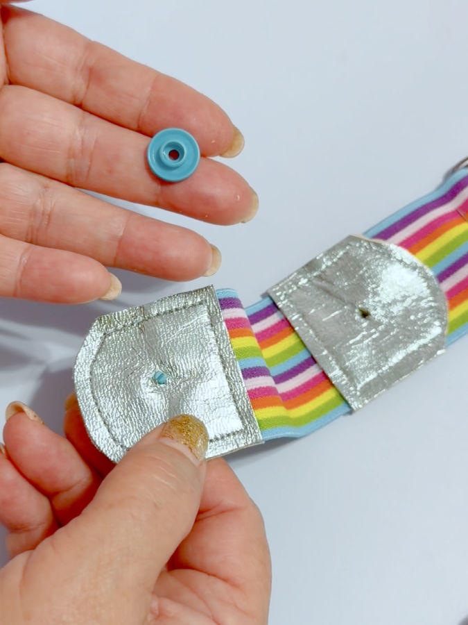 a woman holds in one hand a part of a snap fastener and in the other hand the piece of belt with the prepared hole for snap instrallation