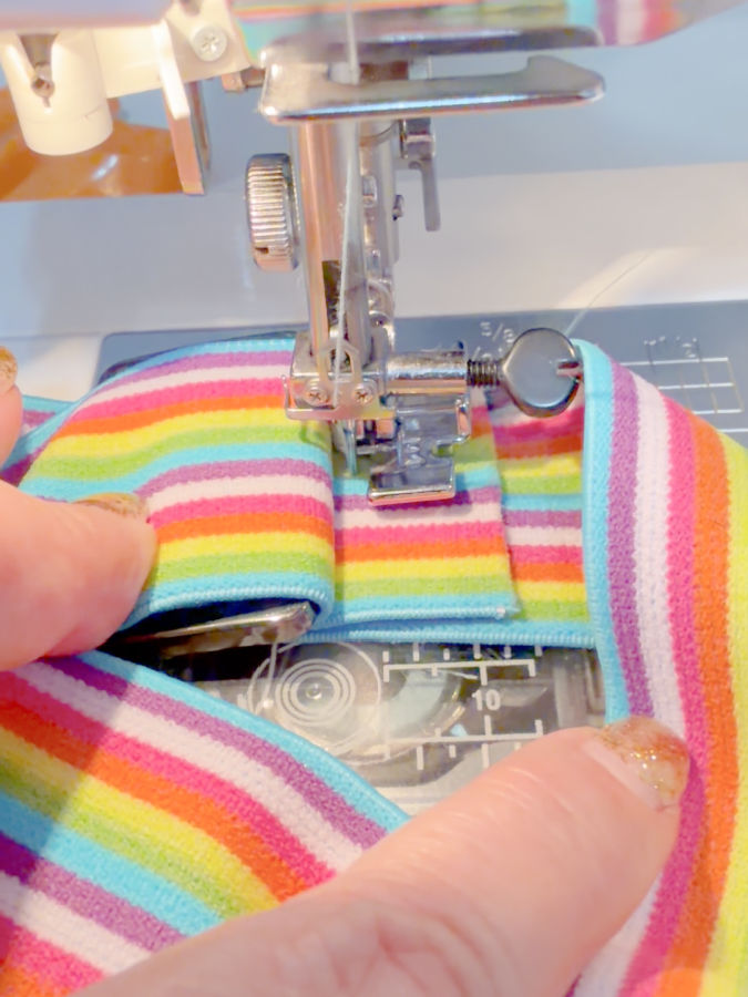 a woman holds with her fingers the elastic while stitching it at a sewing machine