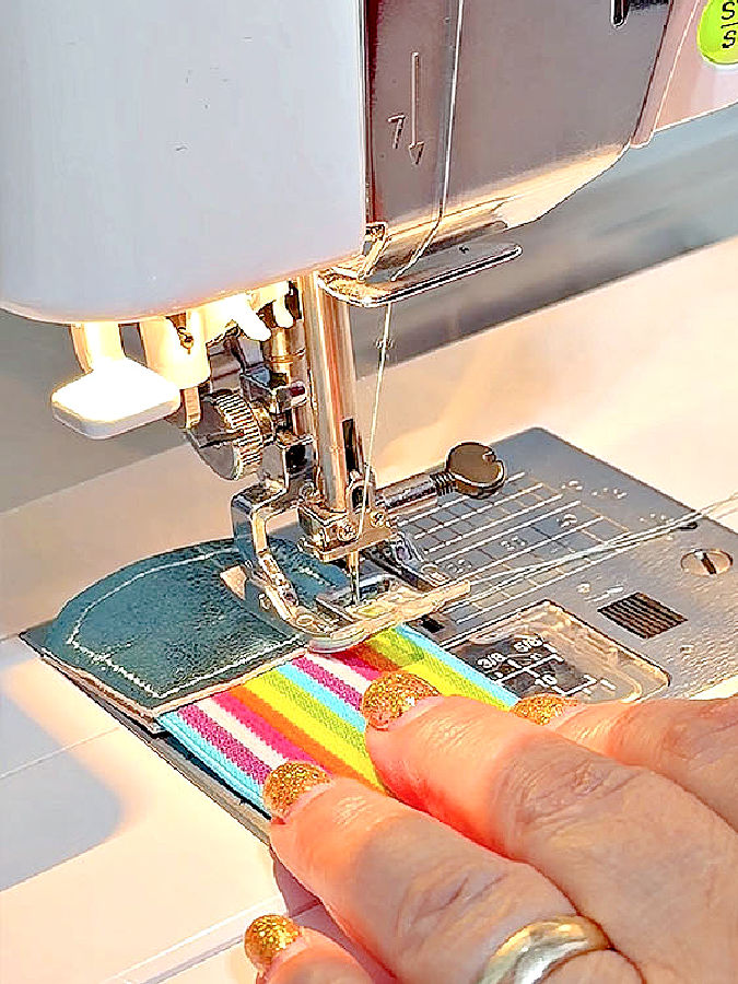 a womans hand holding the piece of leather while sewing on the sewing machine