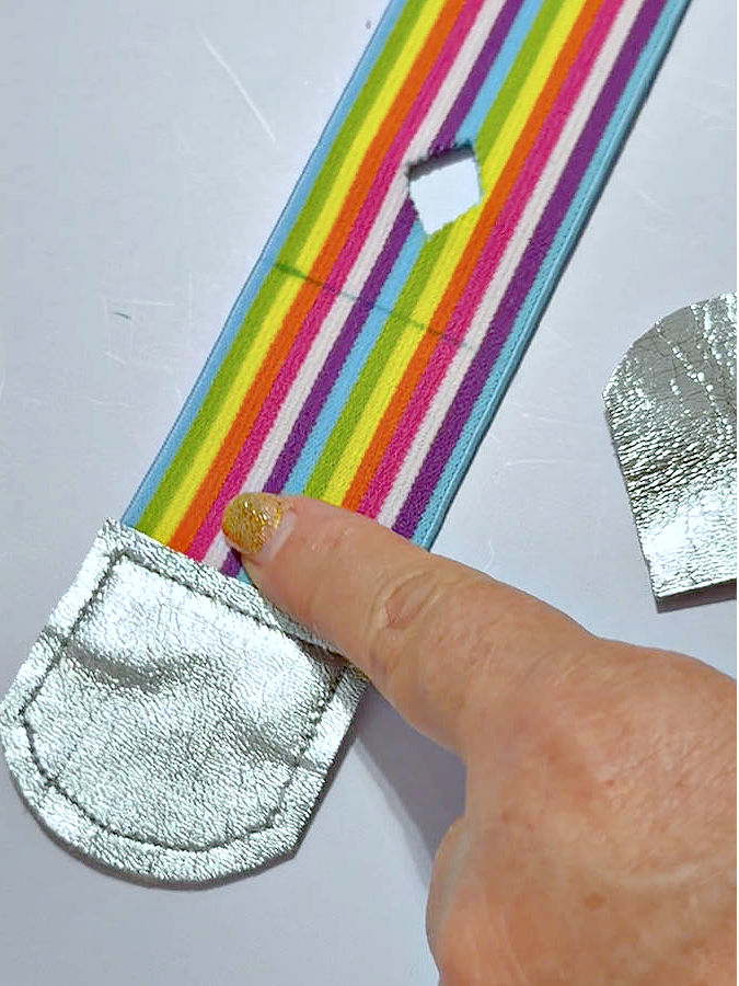 a womans finger holds down a piece of elastic with a small square cut in it where the snap will be installed