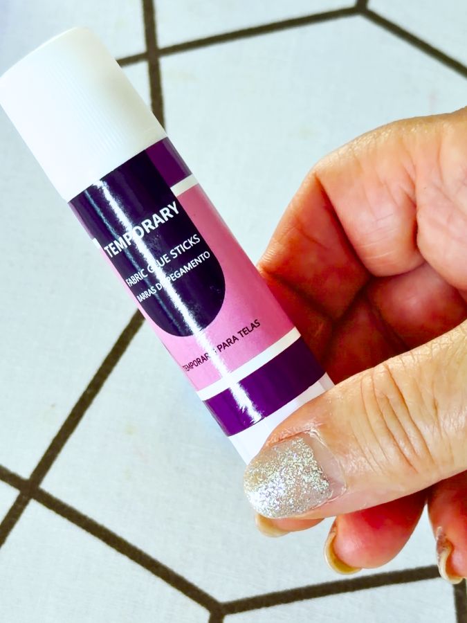 a womans hand holds a stick of temporary fabric glue