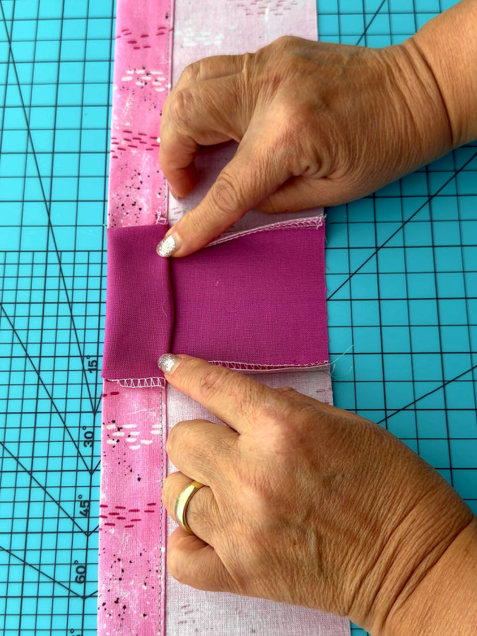 a woman is folding the solid color material over the hem of the already finished piece