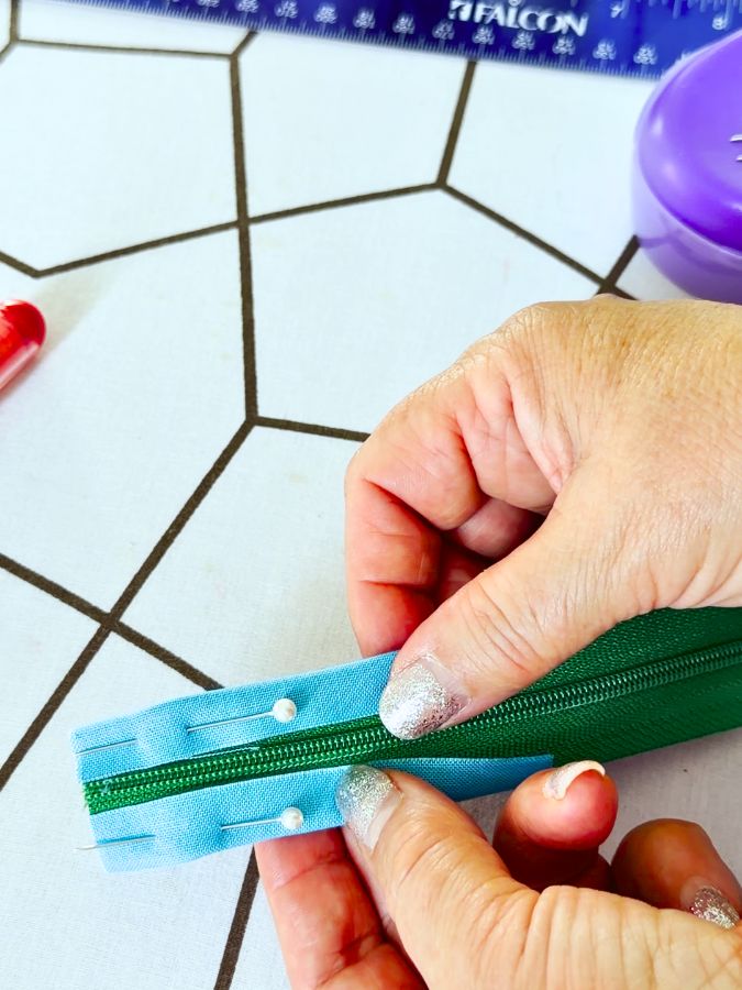a woman holds in her hands the zipper over which the fabric rectangle is folded and pinned