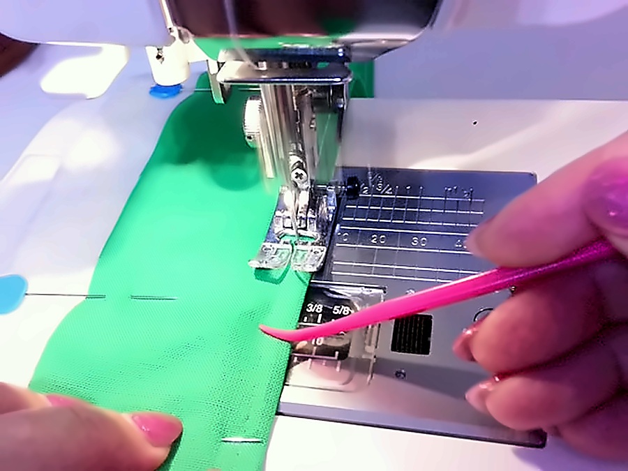 a womans hand uses the purple thang to guide a piece of fabric on a sewing machine