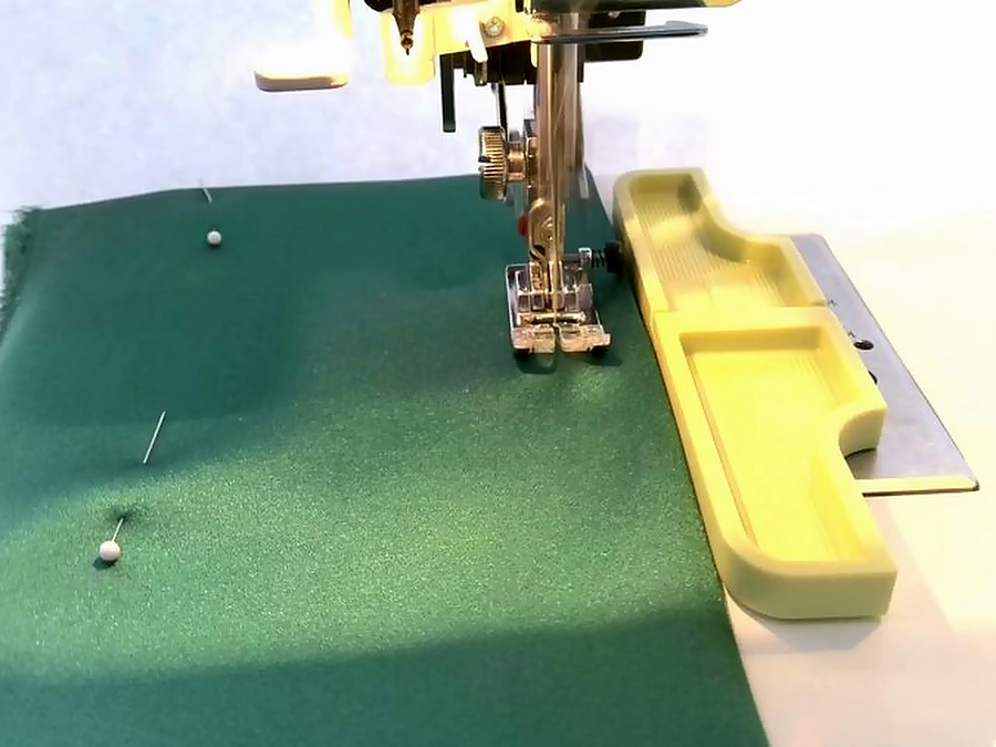 close-up of a sewing machine while sewing a piece of material a seam guide at the right of the needle