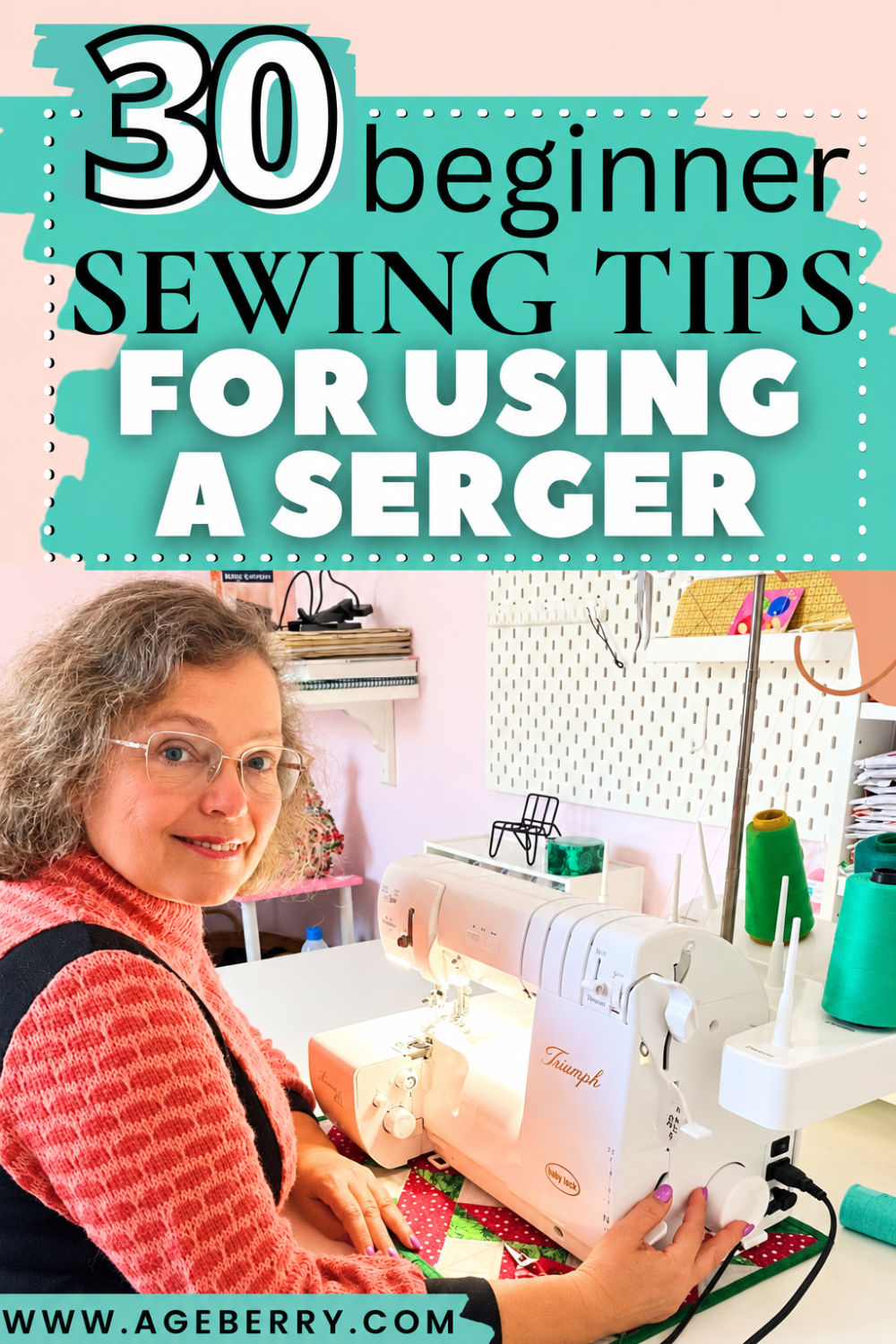 Woman in a coral sweater sitting at a sewing table beside a white serger machine, with green thread cones, shelves, and a pegboard in a pink sewing room.