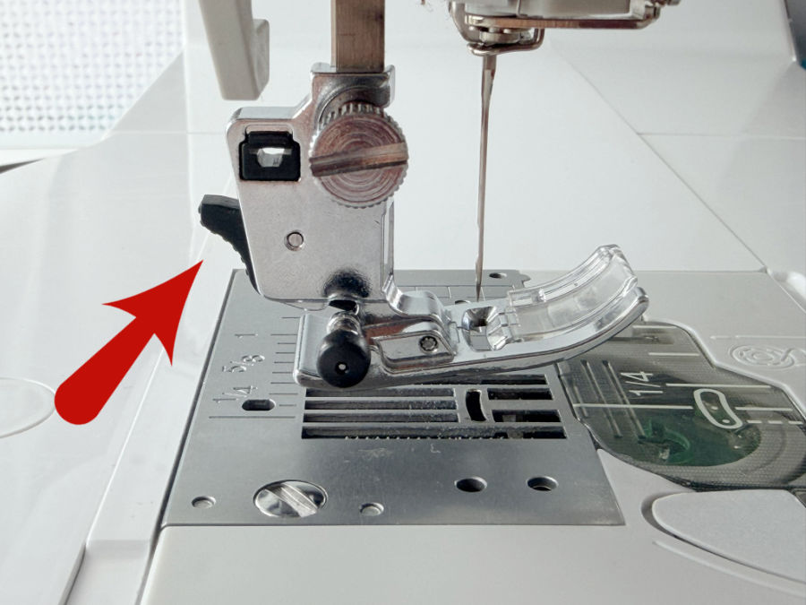 the presser foot of a sewing machine installed in the machine an arrow points to the foot release lever