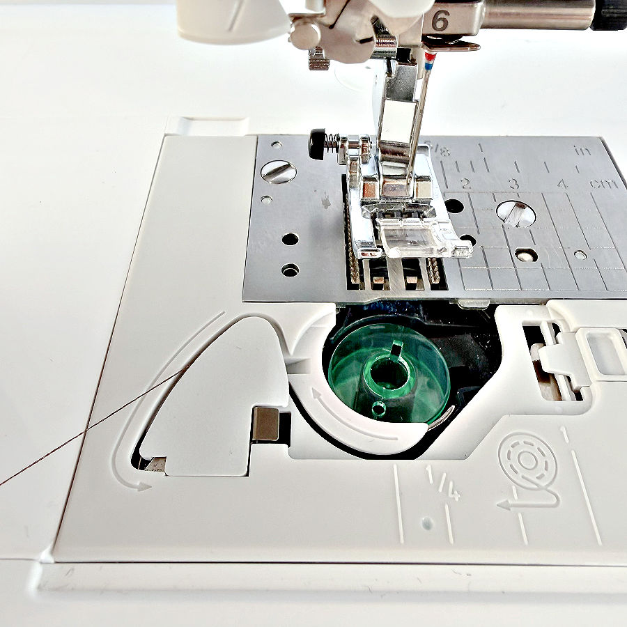 the drop in bobbin area with the cover removed the bobbin is visible and the wire from the bobbin goes to the cutter