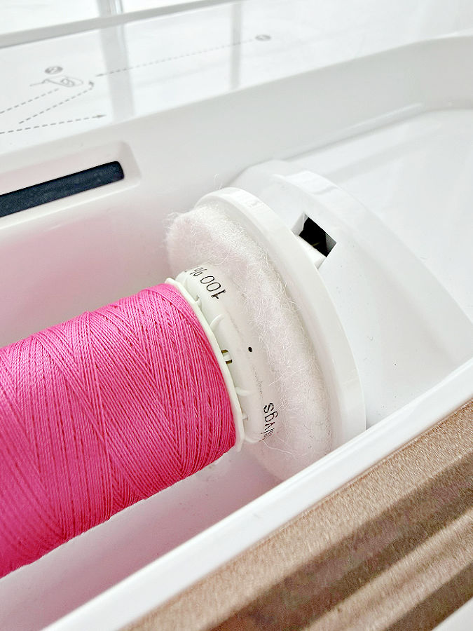 a thread spool mounted on a horizontal pin a felt pad visible between the spool and the sewing machine body