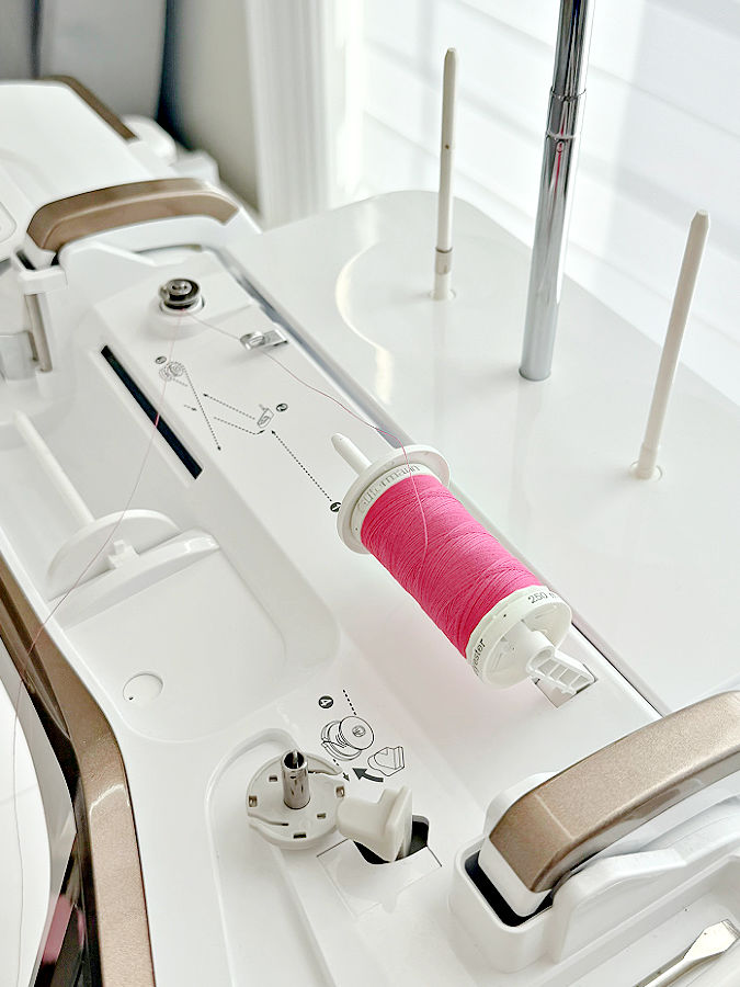 image of the top of a sewing machine with a second horizontal spool pin raised and a spool inserted the thread routed for the bobbin winder