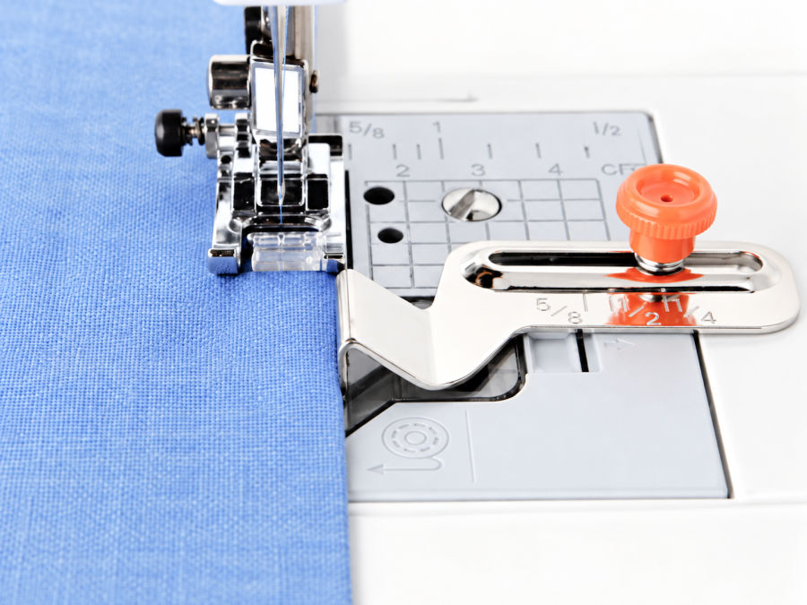 a close up image of an adjustable seam guide mounted with a screw in one of the holes in the needle plate of the machine