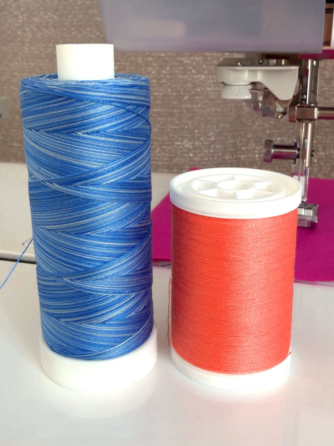 one parallel wound spool and one cross wound spool shown side by side a sewing machine needle assembly in the background