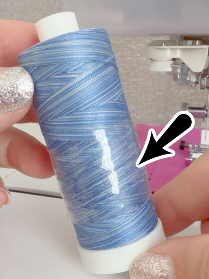 a woman holds a spool of thread with hugos amazing tape wrapped around it an arrow points to the tape