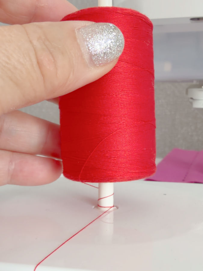 w womans handholds a spool of thread without a wide lower flange and the thread has fallen on the sewing machine pin