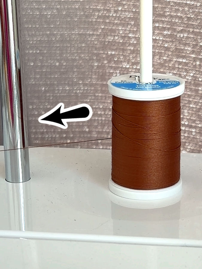 a spool of parallel wound thtread injstalled on a sewing machine an arrow points to the direction the thread is pulled by the machine