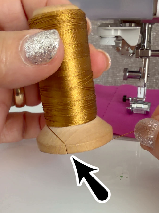 a woman holds a spool of thread between her fingers the base of the spool has a small cut