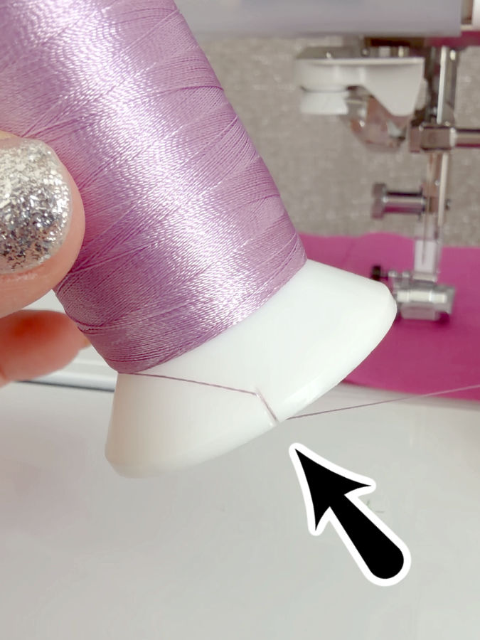 a woman holds a spool of thread between her fingers the base of the spool has a small cut