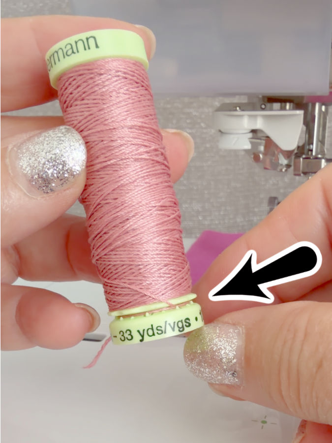 a woman holds a spool of thread an arrow points to a narrow gap at the base of the spool