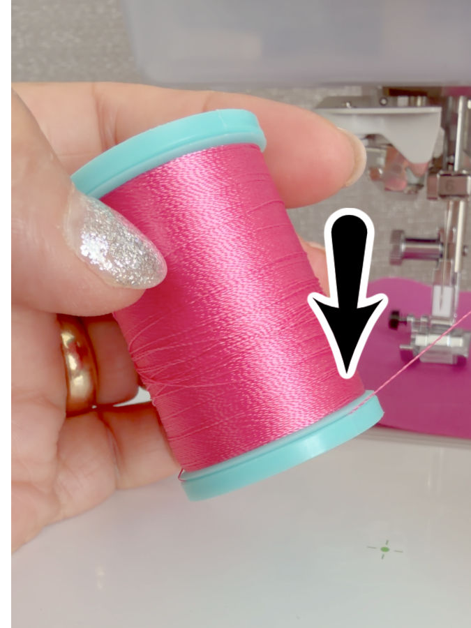 a woman holds a spool of thread an arrow points to a very narrow gap on the base of the spool